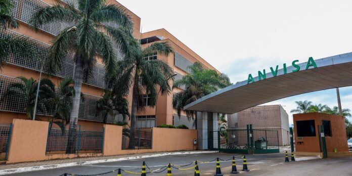 Entrance to the ANVISA building with orange walls, palm trees, and a curved canopy reading ANVISA at the entrance.