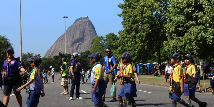 Group of young scouts in uniform walking along a city street with Sugarloaf Mountain visible in the background during a parade.