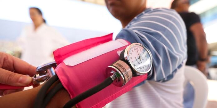 Close-up of an arm in a pink blood pressure cuff with a gauge, as a clinician checks blood pressure.