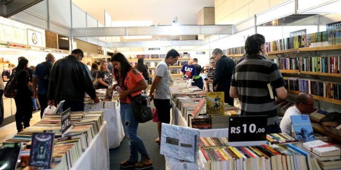 Crowded indoor book fair with tables full of books and people browsing.