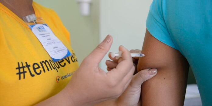 Healthcare worker in a yellow shirt administers a vaccine to a patient with a teal shirt.