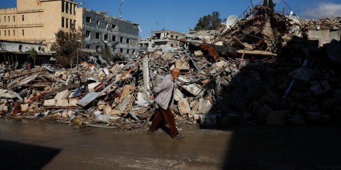 Man with a light jacket walking through a chaotic rubble field of collapsed buildings in a war-torn urban area, blue sky above pmaybe sunny day