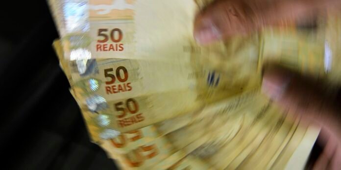 Blurred photo of a hand fanning multiple 50 reais banknotes, motion blurred to suggest cash handling
