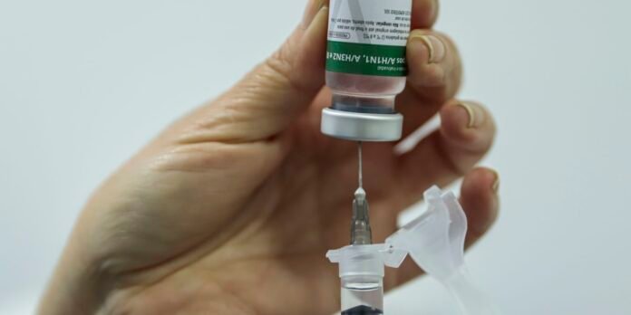 Close-up of a hand drawing liquid from a vial into a syringe for injection.
