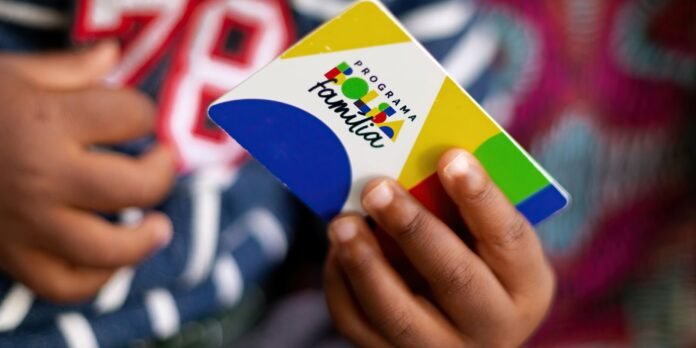 Close-up of a child's hands holding a colorful square card labeled 'Programa Família' with geometric shapes and bold colors.