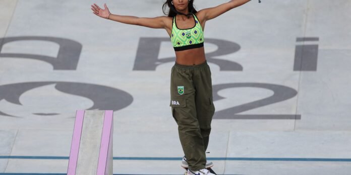 Young woman in a neon green sports bra and olive cargo pants stands with arms outstretched on a concrete skatepark surface with large letters behind her.