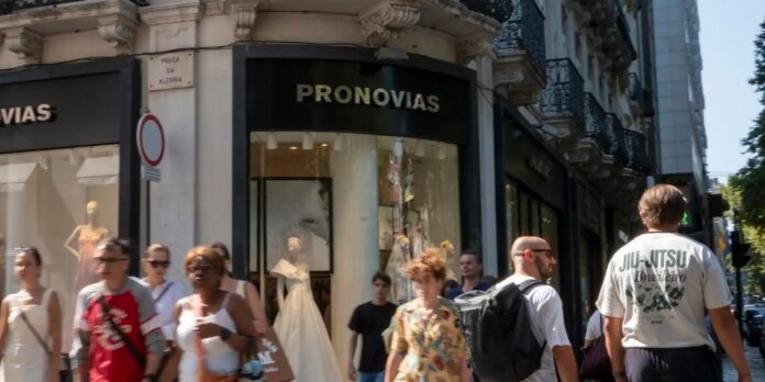 City street scene in front of the Pronovias wedding dress shop; mannequins in wedding gowns visible in the display window.