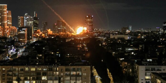 Nighttime city skyline with a large orange explosion near the center, flames and smoke rising above buildings.