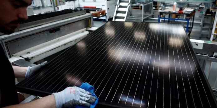 Worker in gloves wipes a large solar panel on a production line, factory tools and equipment in the background