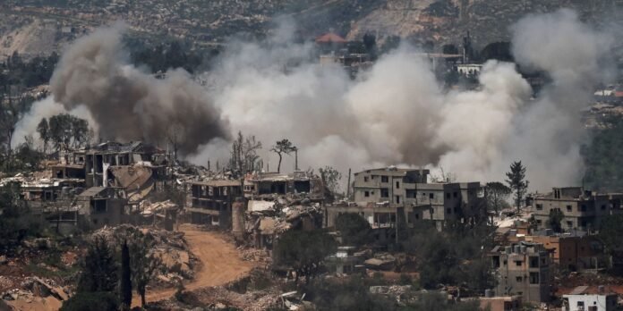 Rubble-strewn hillside town with large smoke plumes rising from destroyed buildings nearby offseason.