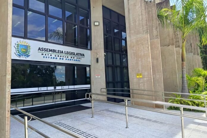 Entrance to the Assembleia Legislativa building in Mato Grosso do Sul, with glass doors, concrete pillars, and a ramp. Palms line the side.
