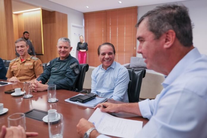Group of officials in a boardroom seated around a table, smiling, with uniformed and civilian men and a woman in background.