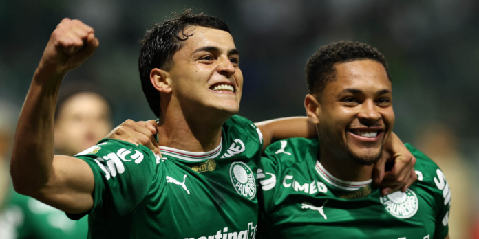 Two Palmeiras players celebrate together on the field, arms around each other, smiling after a goal.