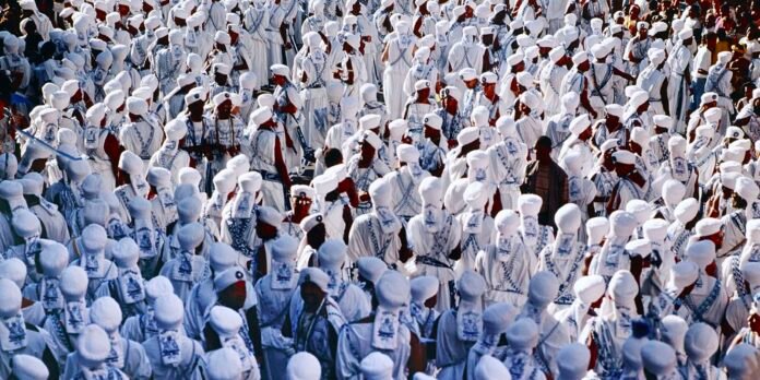 Large crowd of people dressed in white robes and turbans gathered together, likely during a religious pilgrimage.