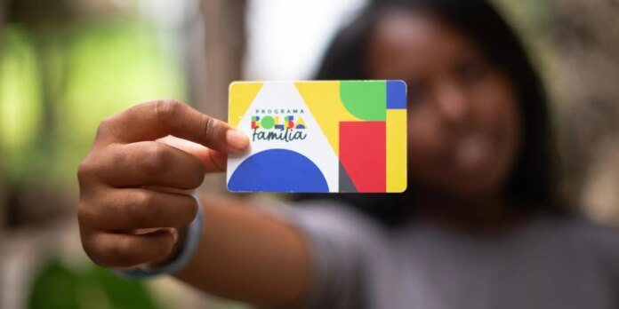 Person holding a colorful Bolsa Família benefits card up to the camera, logo clearly visible.
