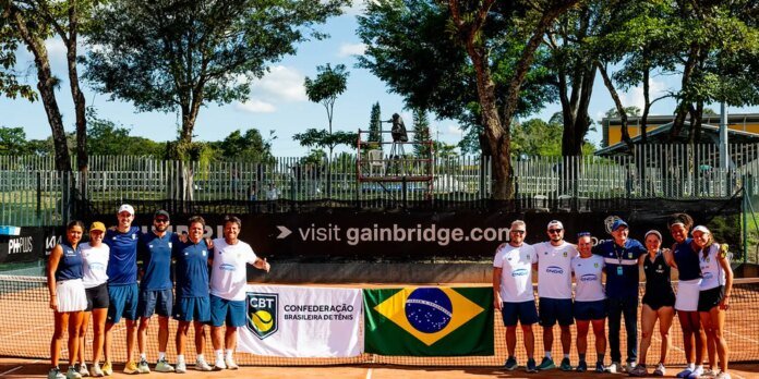 Group of tennis players posing together on a clay court with banners, including the Brazil flag and CBT logo in the foreground.