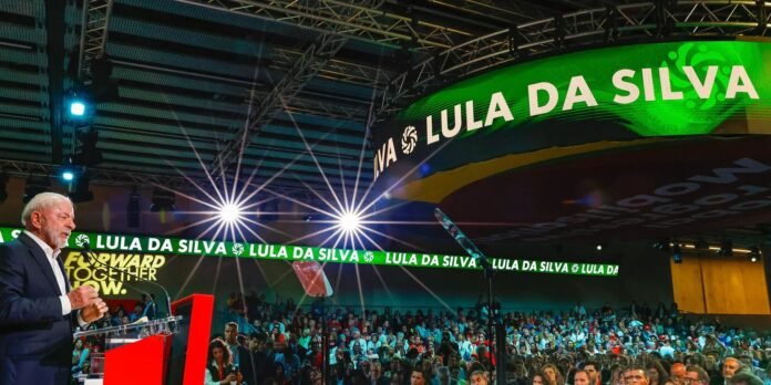 Lula da Silva speaks at a podium on a crowded stage with green banners reading LULA DA SILVA.