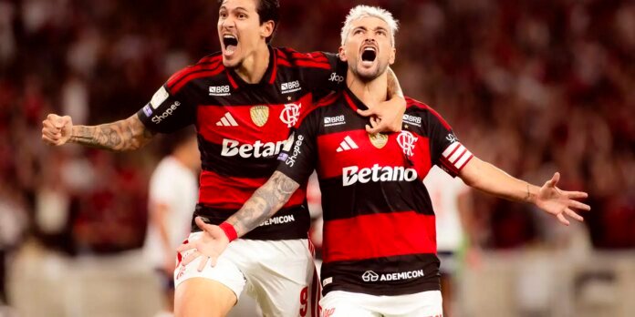Two Flamengo players in red-and-black jerseys celebrate a goal with arms around each other on the pitch.