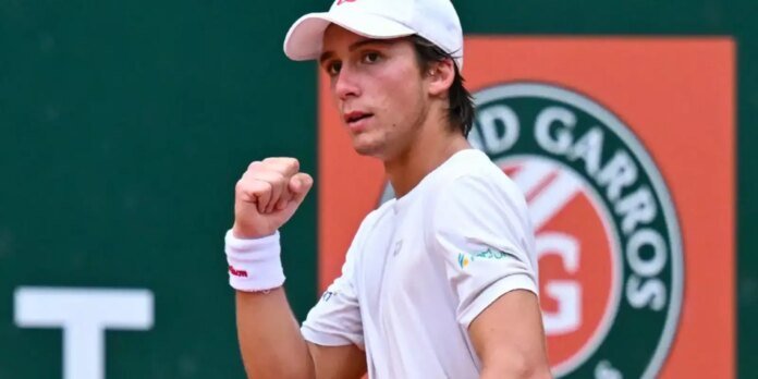 Tennis player in a white cap and shirt raises a clenched fist in celebration on the court.