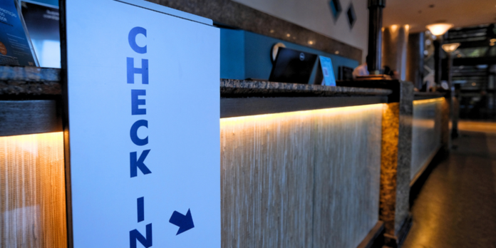 Close-up of a check-in counter with a vertical blue 'CHECK-IN' sign on the left and warm backlit panel along the front of the desk.