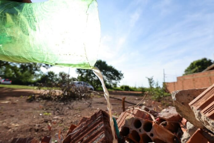 Green plastic bottle pouring water onto a pile of bricks and rubble in an outdoor construction area under a blue sky.