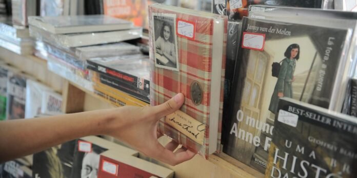 Person's hand reaches to grab a plaid-covered diary on a bookstore shelf beside vinyl records and other books on display.