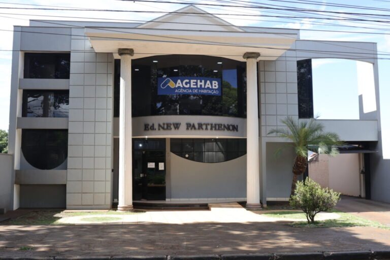 Front view of a modern office building with two tall columns and a curved entrance, showing signage for AGEHAB Agência de Habitação and Ed. New Parthenon