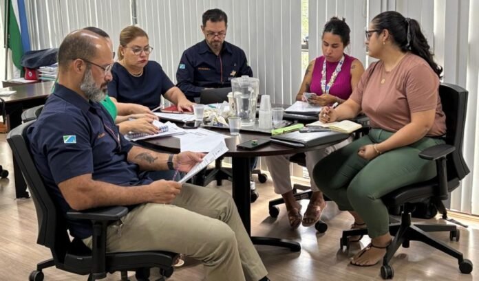 Six colleagues around a round table in a bright office, reviewing documents and taking notes.