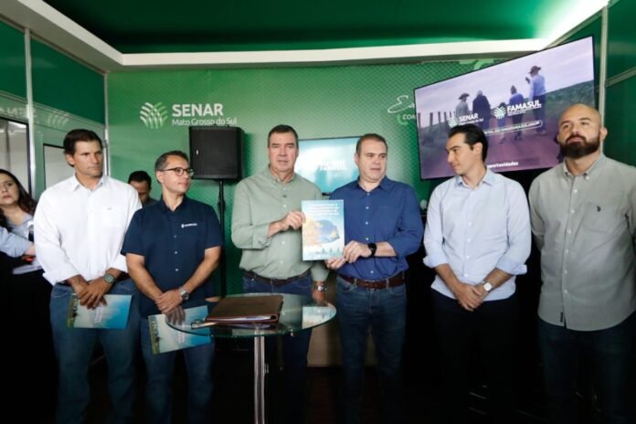 Group of men in business casual attire at a presentation, exchanging a booklet in front of a green SENAR backdrop.