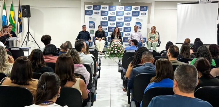 Panel discussion in a conference room with six panelists on a dais, a flower arrangement in front, and an audience facing them.