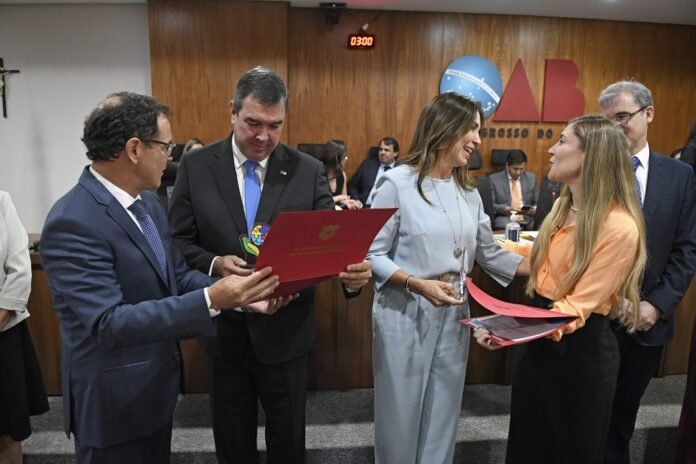 People in business attire exchange documents during a formal award ceremony in a wood-paneled room.