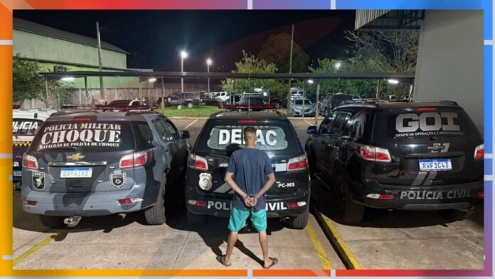 Person wearing a blue shirt and green shorts stands with hands behind back between three police vehicles at night in a parking lot (Polícia Civil/Choque/GOI).