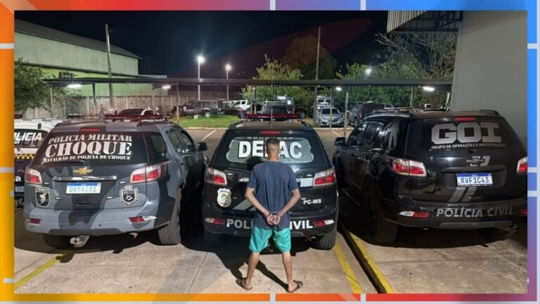 Person wearing a blue shirt and green shorts stands with hands behind back between three police vehicles at night in a parking lot (Polícia Civil/Choque/GOI).