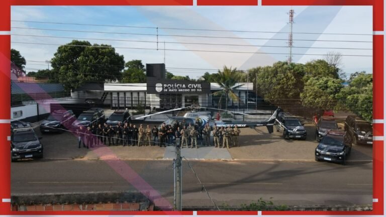 Group of police and military personnel posing in front of a Polícia Civil de Mato Grosso do Sul building, with several patrol vehicles and a helicopter nearby.