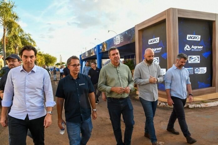 Group of men walking outdoors at an agricultural expo, sponsor banners with iAGRO and Agraer logos in the background.