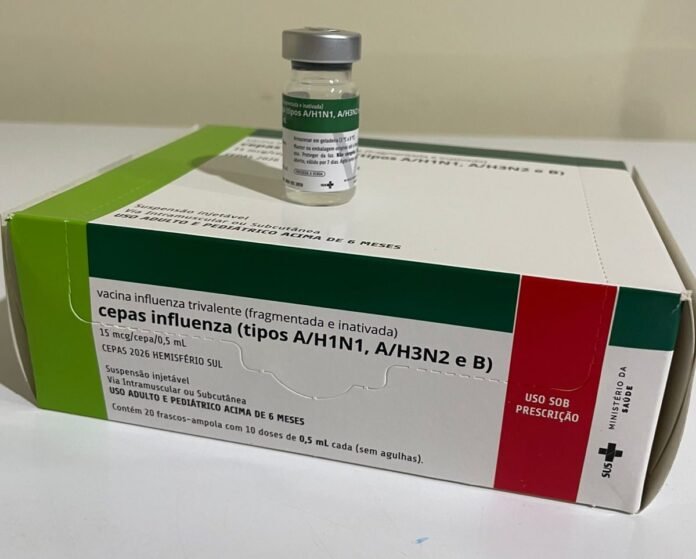 Box labeled with influenza vaccine (types A/H1N1, A/H3N2 and B) and a small vial resting on top against a white surface, green and white packaging with a red panel on the side.