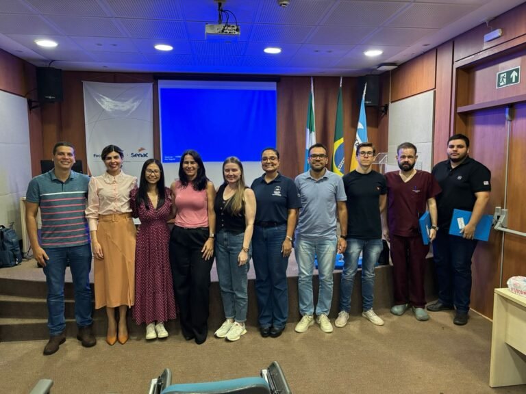 Group of ten people standing side by side on a stage in a conference room, posing for a photo with a blue screen behind them and flags in the background