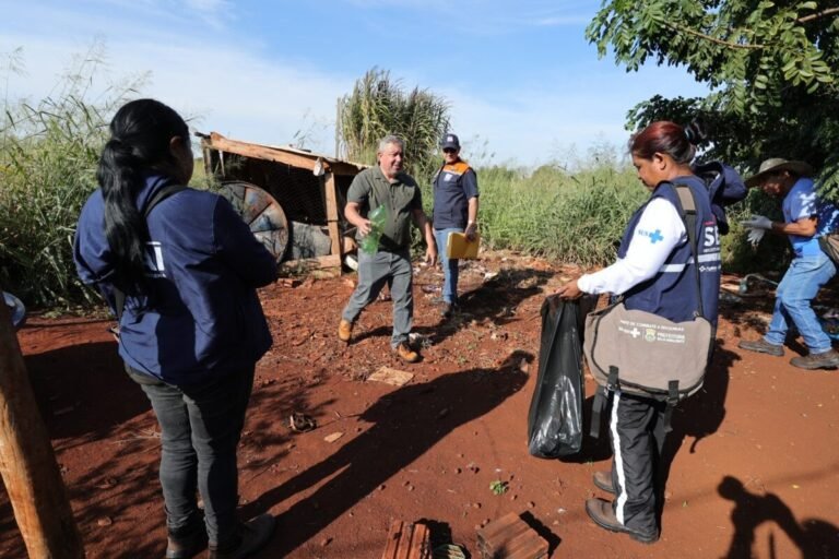 Group of volunteers and responders in a dusty outdoor area, collecting trash and placing it in bags near a dilapidated machine.