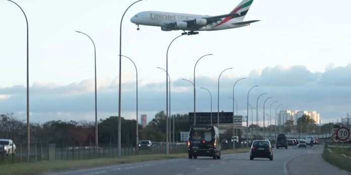 Emirates airplane descending over a busy highway with cars and curved streetlamps beneath it.