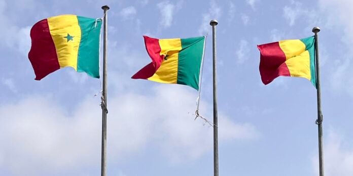 Three Senegalese flags fluttering on flagpoles against a blue sky.