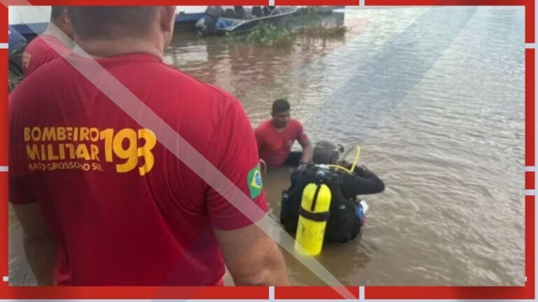 Firefighters in red shirts wade through floodwaters, preparing scuba gear for a water rescue.