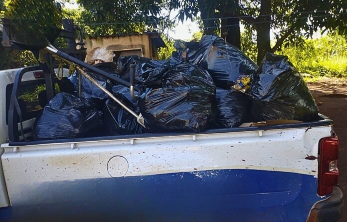 White pickup bed loaded with tied black trash bags under trees, ready for disposal.