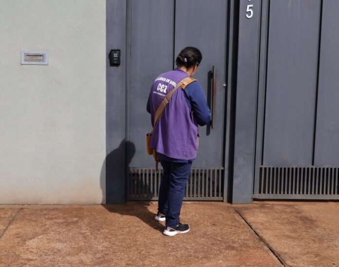 Person seen from behind in a purple shirt and dark jeans, reaching for a tall gray door marked with the number 5 on a sidewalk.