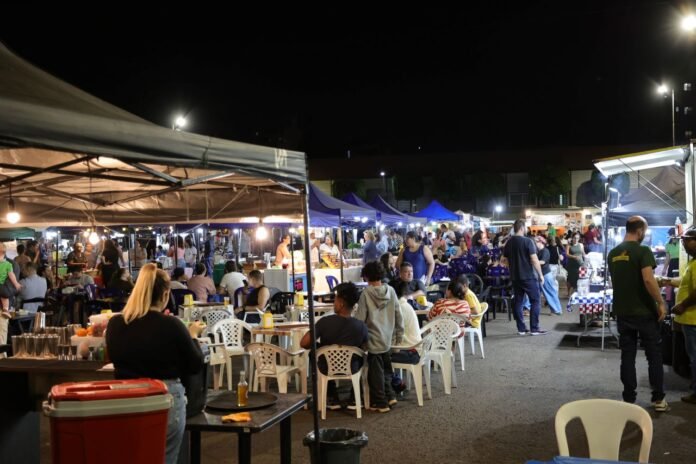 Night market scene with food stalls under colorful tents, string lights, and people dining at plastic tables. (informative)