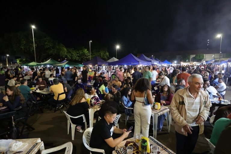 Night market scene with numerous tents, string lights, and crowds dining at plastic tables under a dark sky