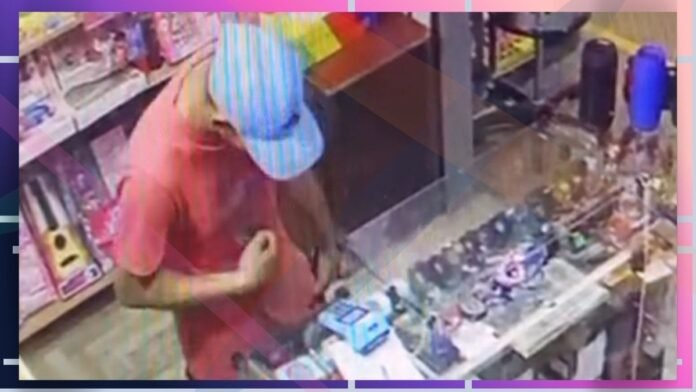Person in a pink shirt and blue striped cap at a store counter, handling items from the display case nearby.