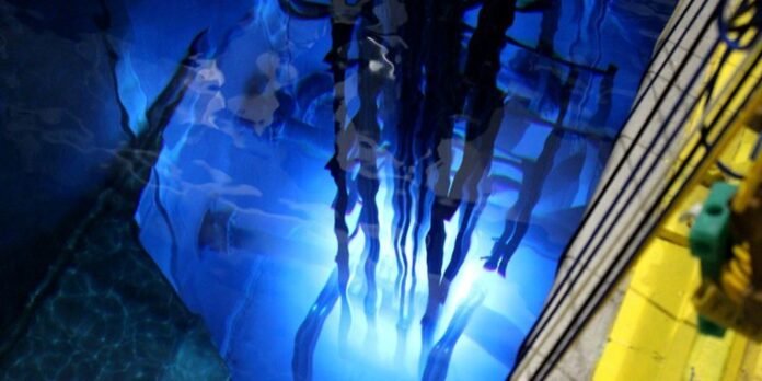 Blue-lit underwater aquarium tunnel with silhouetted divers swimming above and a yellow railing on the right side.
