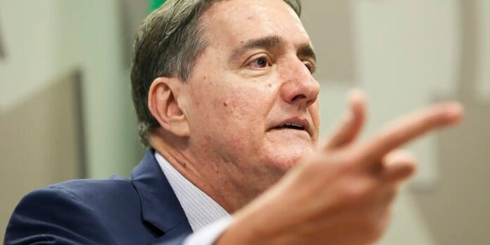 Man in a navy suit speaking and gesturing with his hand in a close-up shot.