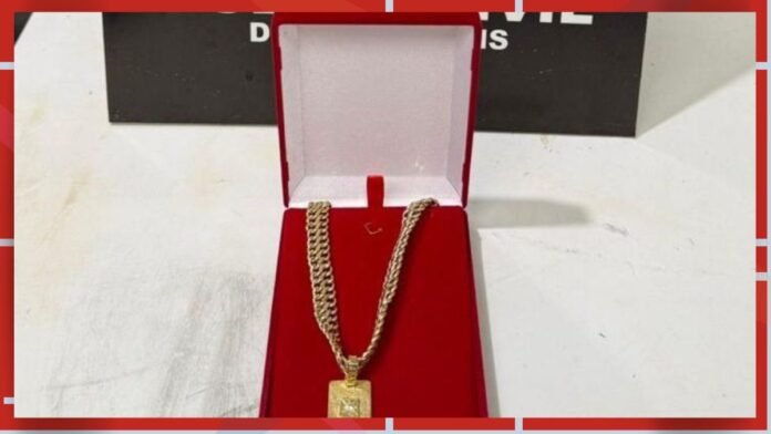 Gold-toned chain necklace with square pendant in an open red jewelry box lined with white fabric.