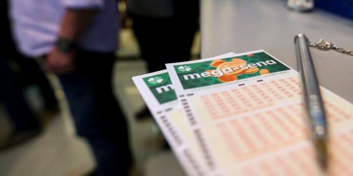 Two Mega-Sena lottery tickets on a counter with a silver pen nearby; blurred people in the background.